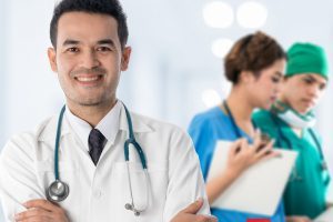 Male Doctor smiling with co-workers in the background.